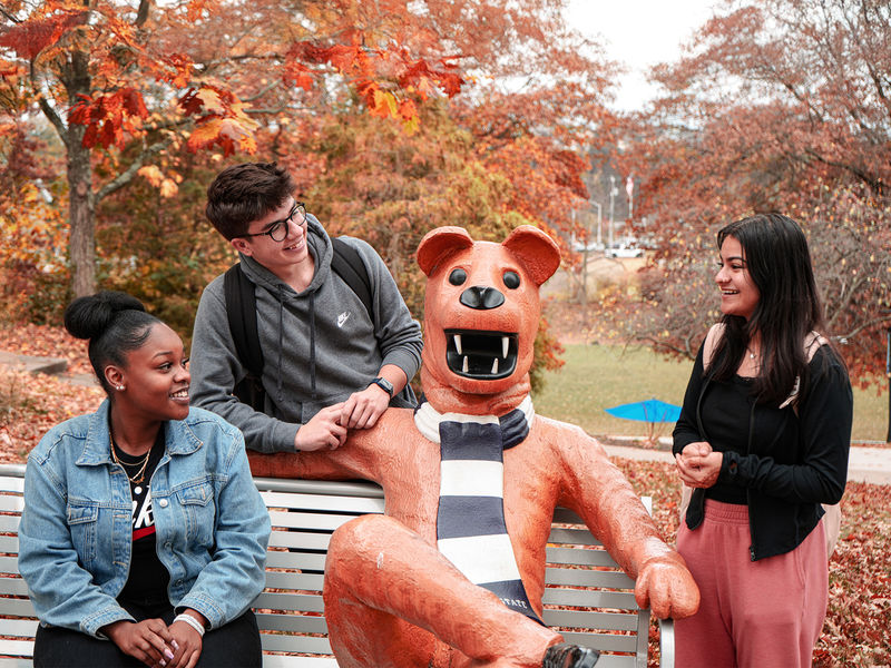 a group of students gather around the nittany lion bench for a photo